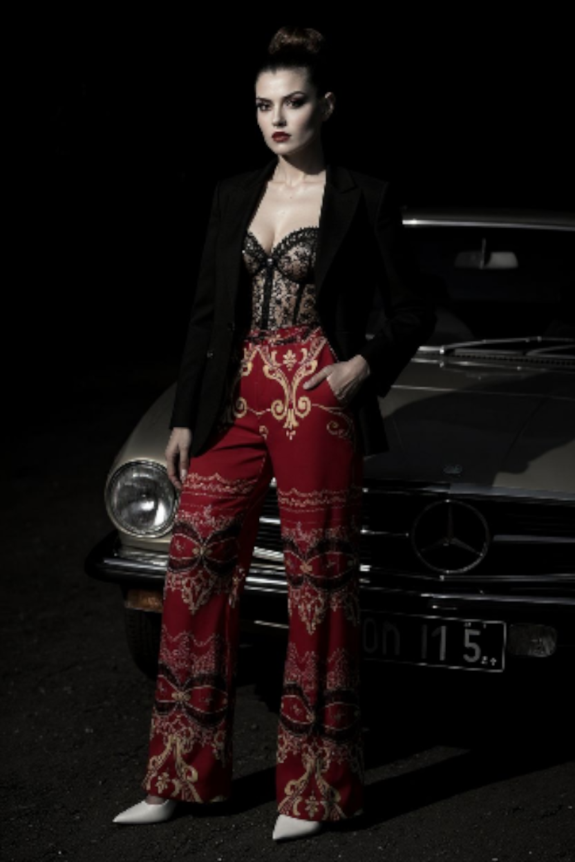 Model wearing burgundy high waist wide leg pants with intricate gold patterns and a black blazer