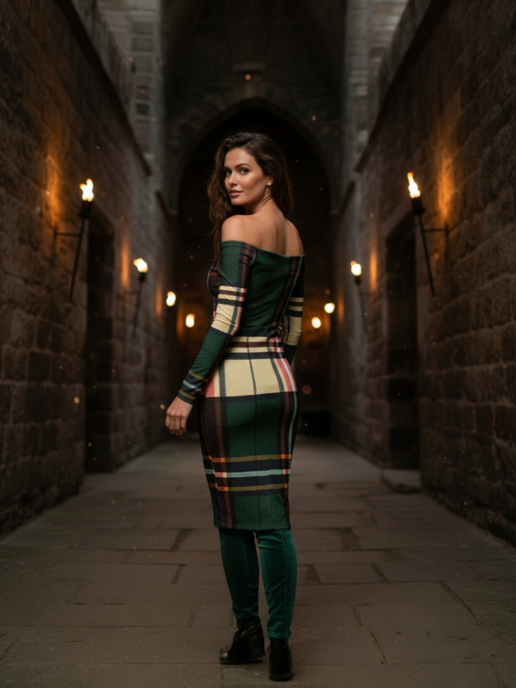 Woman wearing a green tartan off the shoulder midi dress standing in a dimly lit stone hallway