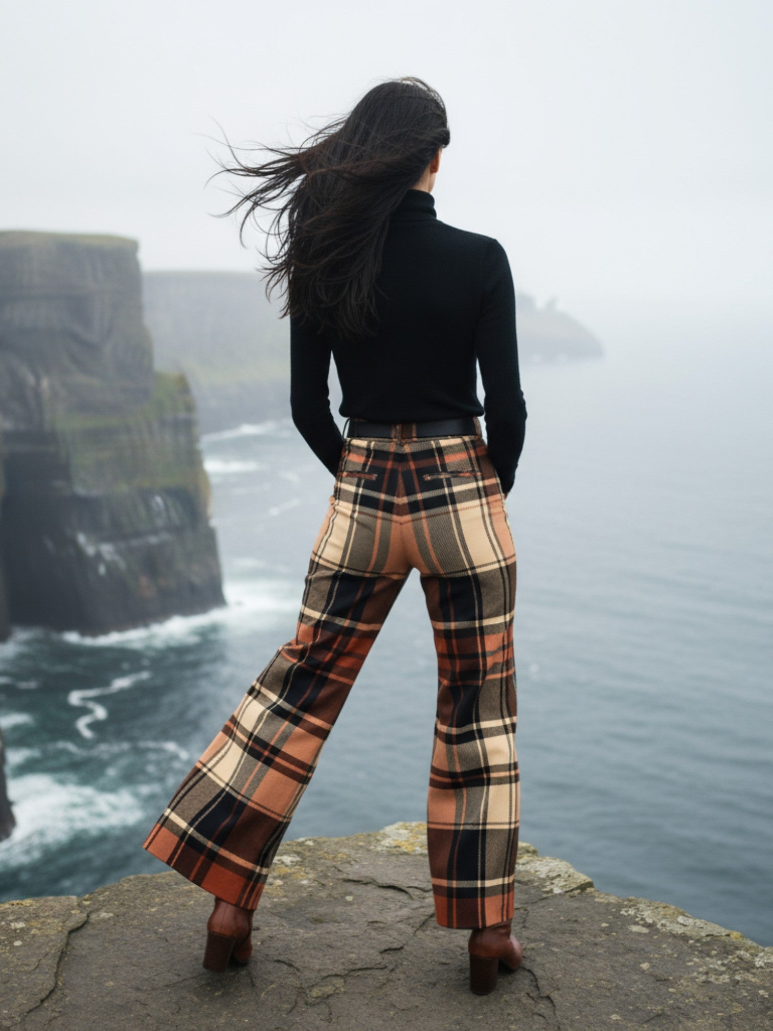 Woman wearing women’s wide leg high waist tartan trousers standing on cliff edge with ocean view