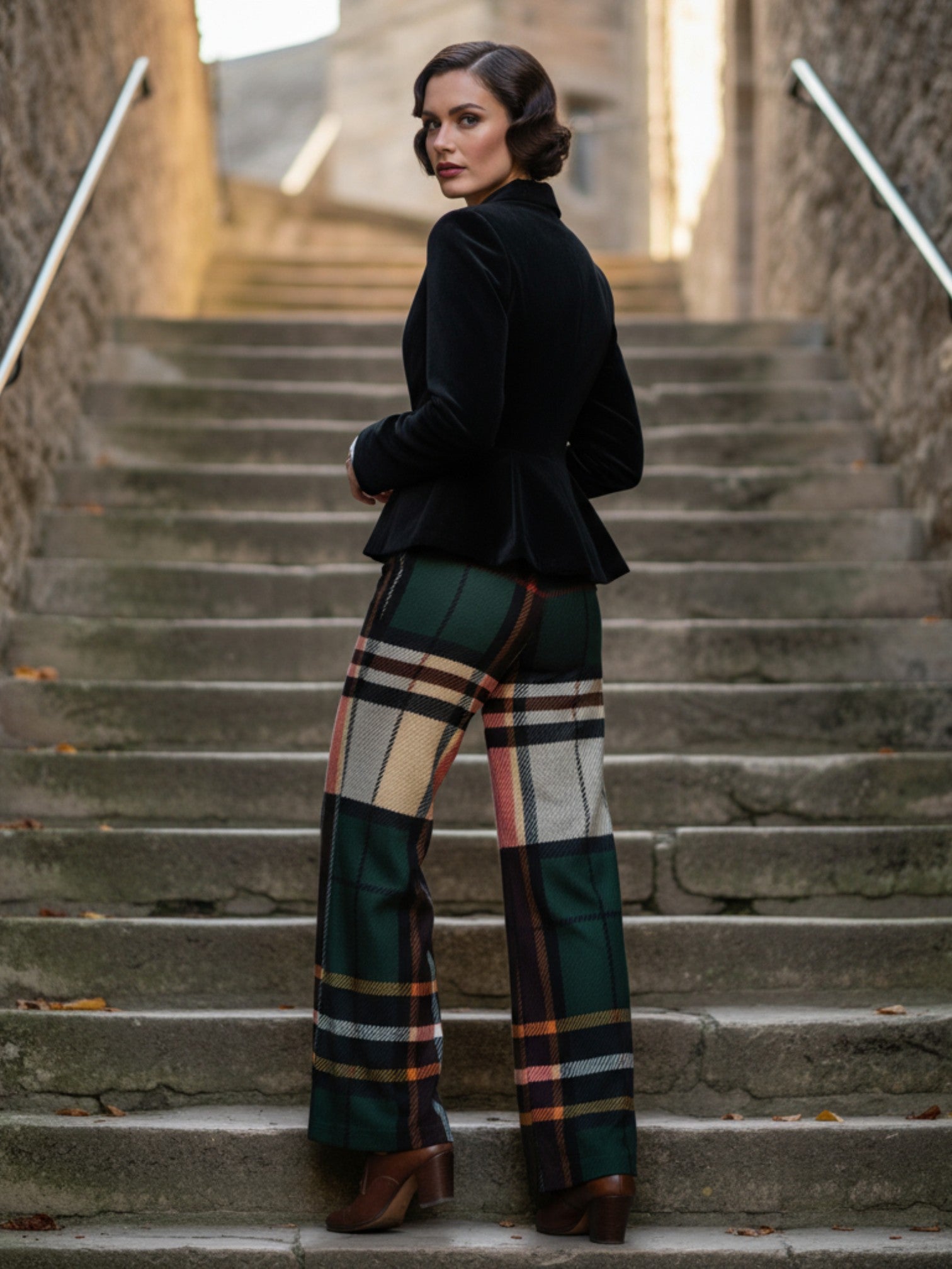 Woman wearing women's tartan wide-leg trousers in green and beige plaid standing on stone stairs
